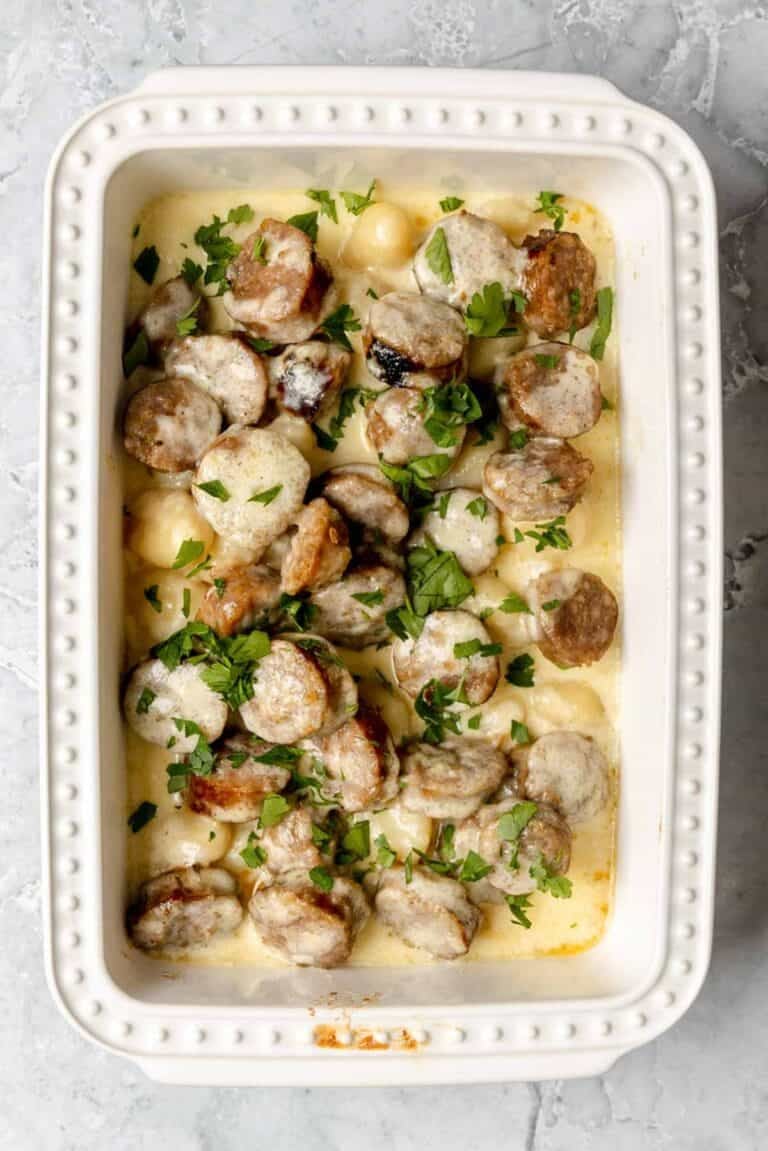 Creamy alfredo sausage and gnocchi bake in a casserole dish on a marble surface.