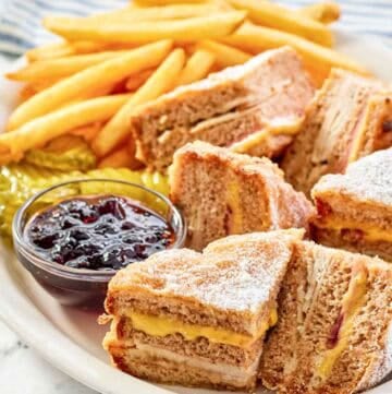 Copycat Bennigan's monte cristo sandwich slices, raspberry jam, fries, and pickles on a platter.