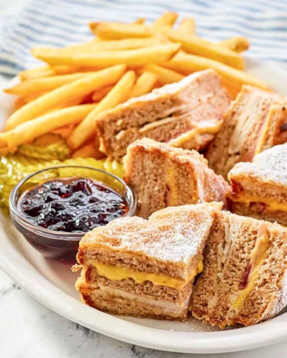 Copycat Bennigan's monte cristo sandwich slices, raspberry jam, fries, and pickles on a platter.