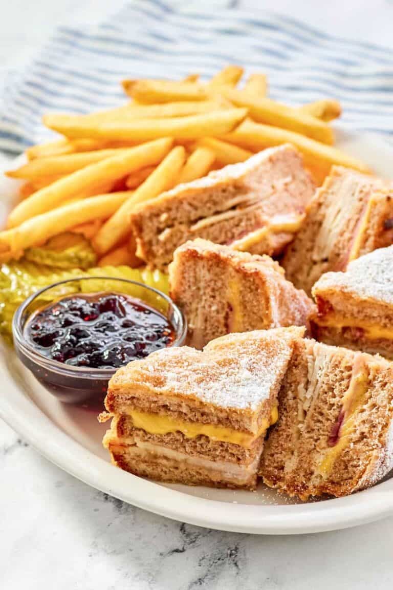 Copycat Bennigan's monte cristo sandwich slices, raspberry jam, fries, and pickles on a platter.