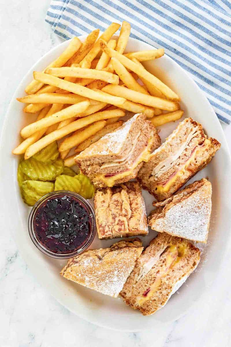 Copycat Bennigan's monte cristo sandwich on a platter with jam, pickles, and fries.