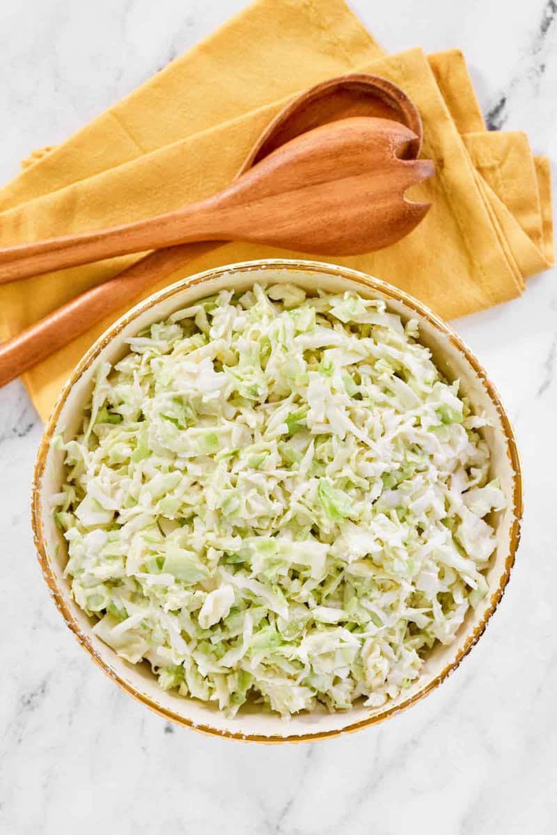 Copycat Brookville Hotel coleslaw in a bowl and wooden salad servers by it.