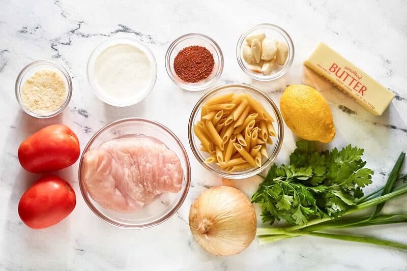 Ingredients for Cajun chicken pasta laid out: chicken, pasta, cream, butter, lemon, tomatoes, onion, and spices.