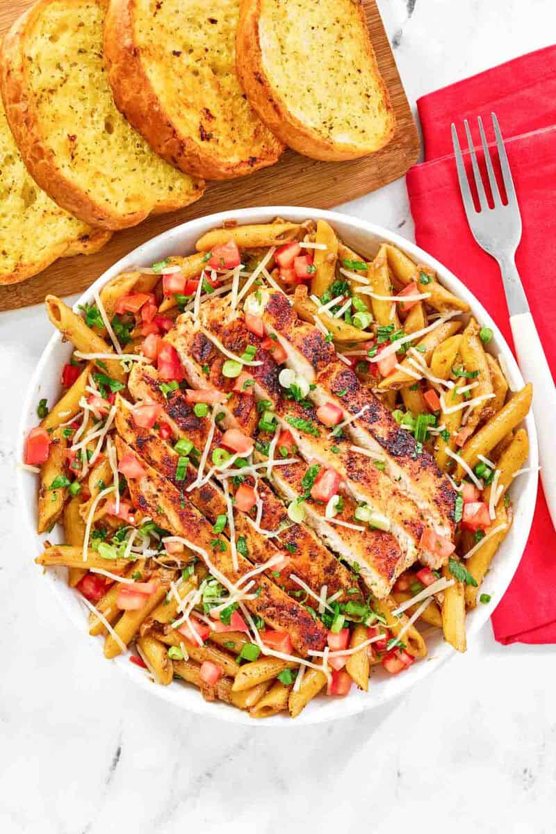 Copycat Chili's cajun chicken pasta, garlic bread, and a fork on a cloth napkin.