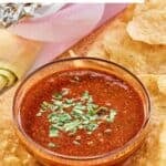 A small bowl of homemade Chipotle red chimichurri sauce with tortilla chips by it.