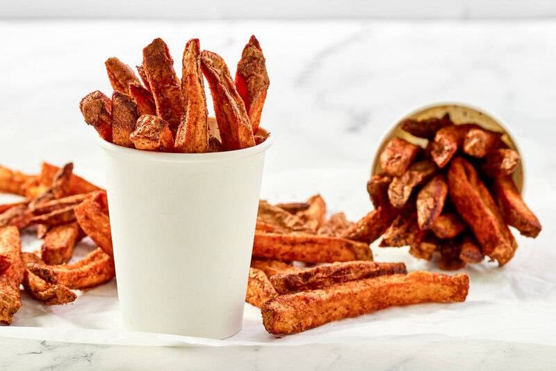 Copycat Five Guys Cajun fries in cups and on parchment paper.