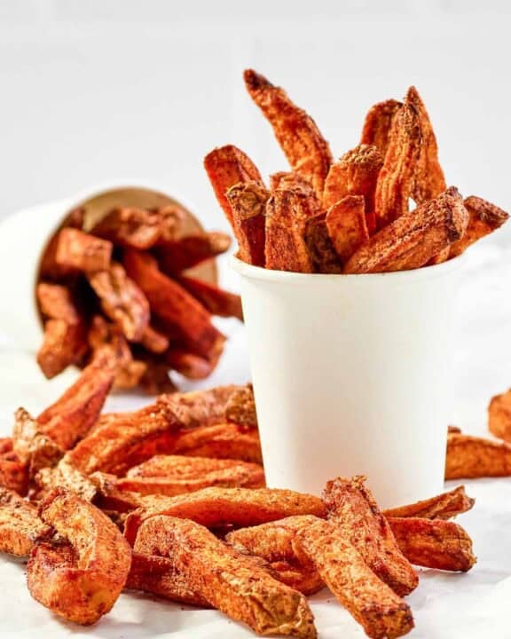 Copycat Five Guys Cajun fries served in large cups and on parchment paper.