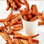 Homemade Five Guys Cajun fries scattered on parchment paper and in serving cups.