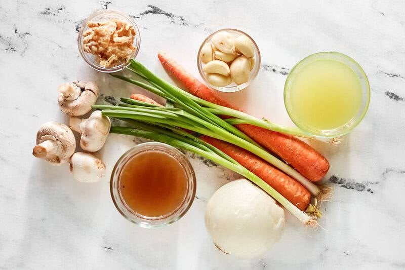 Overhead view of ingredients for Japanese clear soup: broth, carrots, onions, garlic, mushrooms, and fried onions.