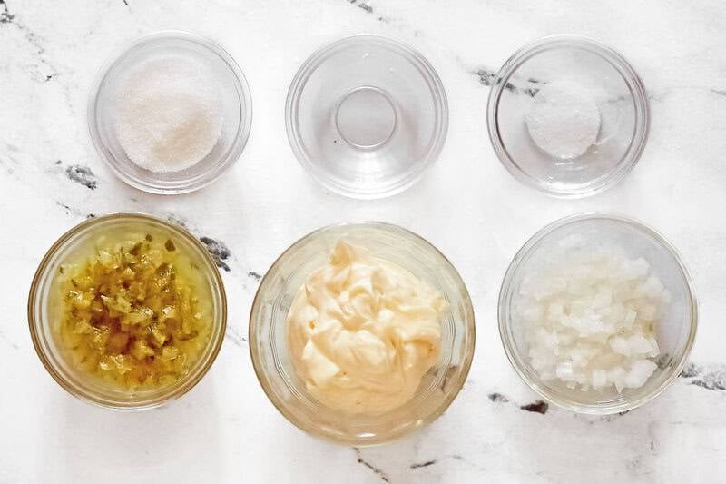 Small bowls containing mayo, chopped white onion, vinegar, pickle relish and more to make tartar sauce.