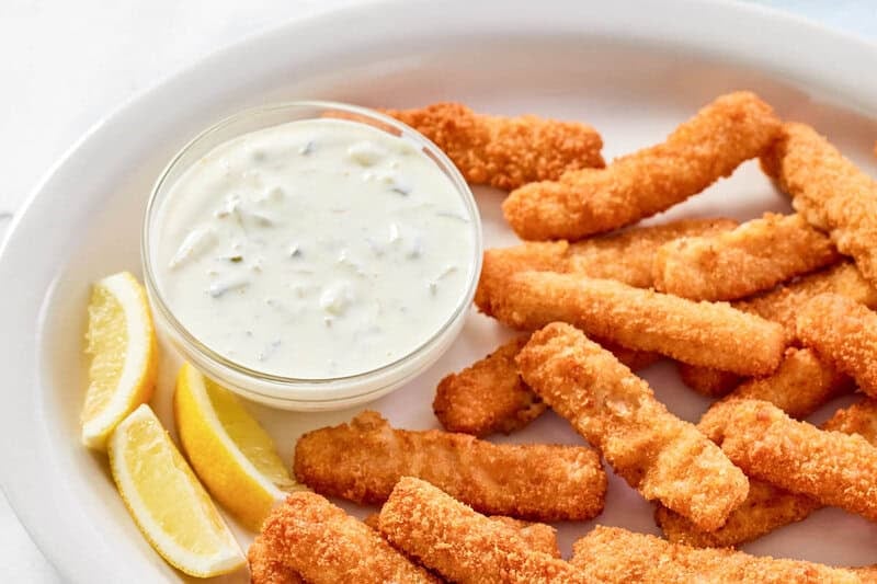 Copycat Skippers tartar sauce in a small bowl, fish sticks, and lemon wedges.