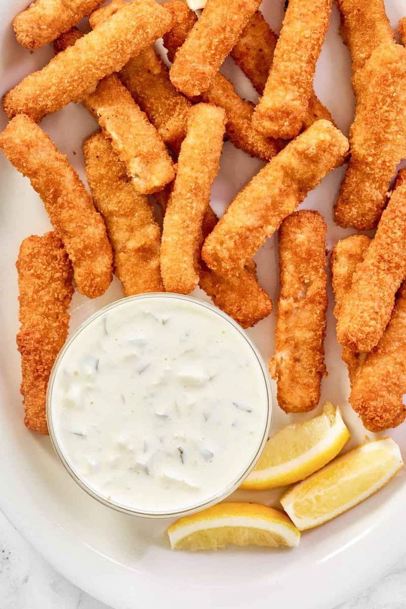 Copycat Skippers tartar sauce, fish sticks, and lemon wedges on a platter.