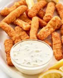 Copycat Skippers tartar sauce in a small bowl, fried fish sticks, and lemon wedges.