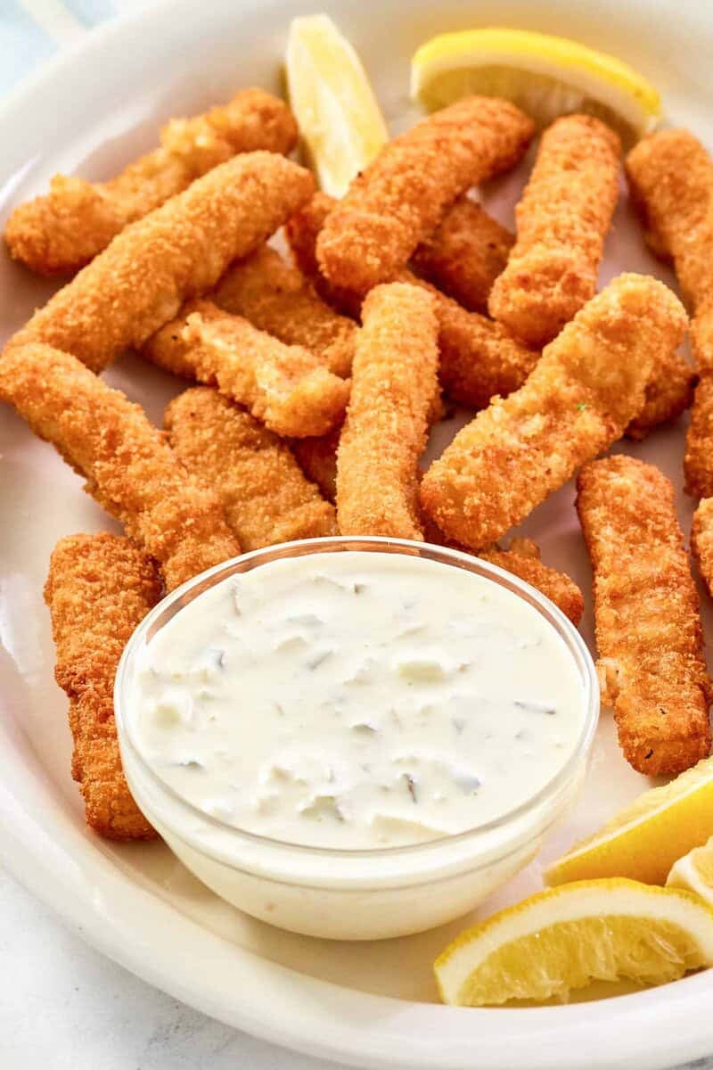 Copycat Skippers tartar sauce in a small bowl, fried fish sticks, and lemon wedges.