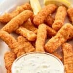 A small bowl of homemade Skippers tartar sauce and fish sticks on a platter.