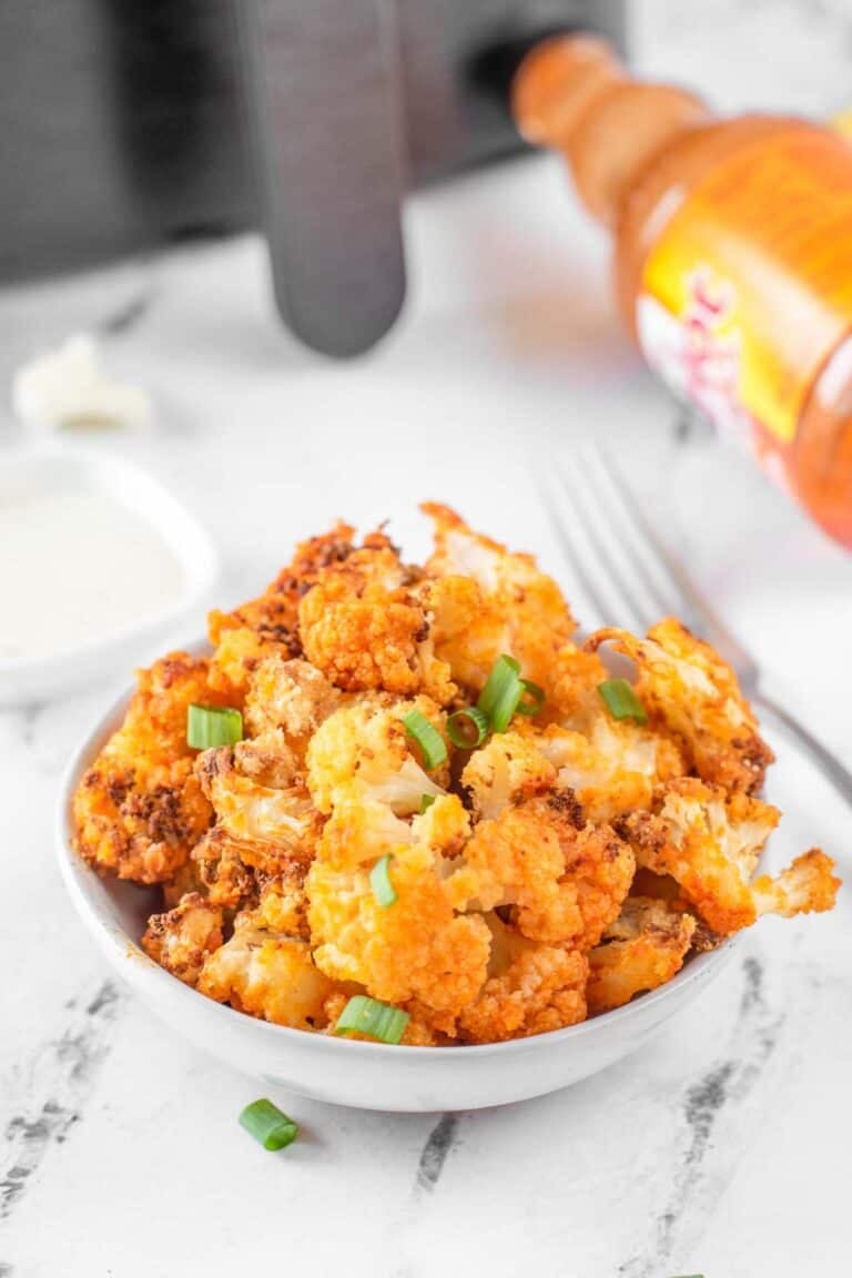 Air fryer buffalo cauliflower garnished with green onions on a marble surface.
