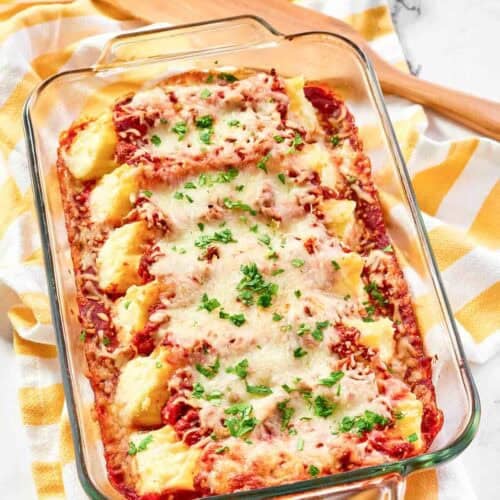 Homemade four cheese manicotti with meat sauce in a baking dish on a kitchen towel.
