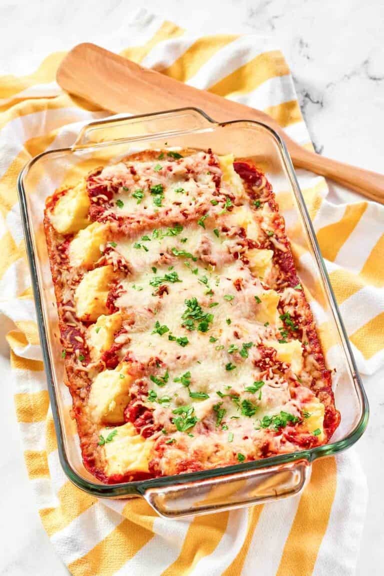Homemade four cheese manicotti with meat sauce in a baking dish on a kitchen towel.