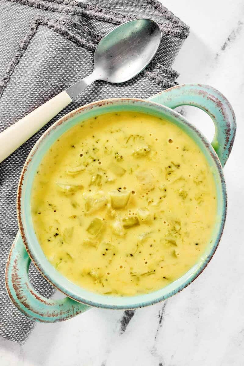 A bowl of copycat Jason's Deli broccoli cheese soup and a spoon on a napkin next to it.