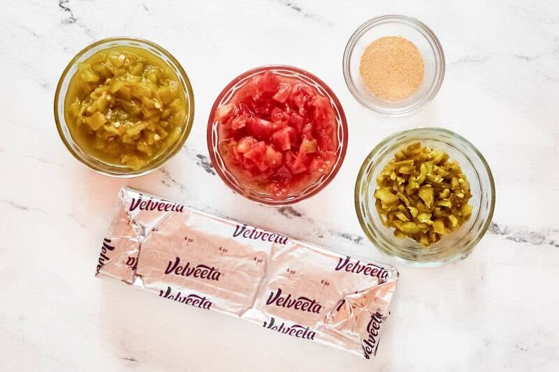 Overhead view of ingredients: Velveeta block, Rotel tomatoes, chopped green chiles, diced jalapeños, and garlic powder.