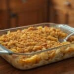 A chicken noodle casserole with wide egg noodles, creamy sauce, and a golden breadcrumb topping baked in a vintage glass baking dish.