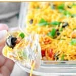 A hand holding a tortilla chip with 7 layer dip on it.