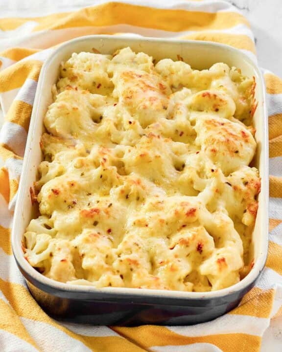 Creamy, cheesy cauliflower au gratin in a casserole dish resting on a kitchen towel.