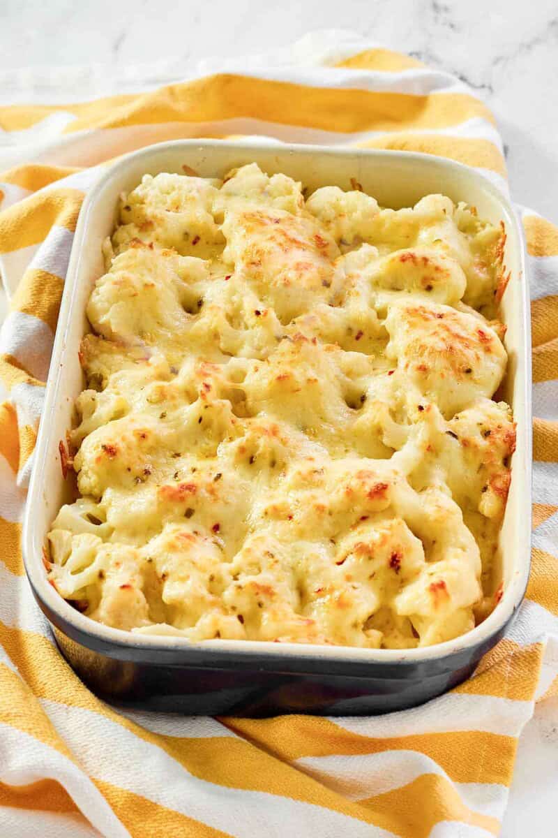 Creamy, cheesy cauliflower au gratin in a casserole dish resting on a kitchen towel.