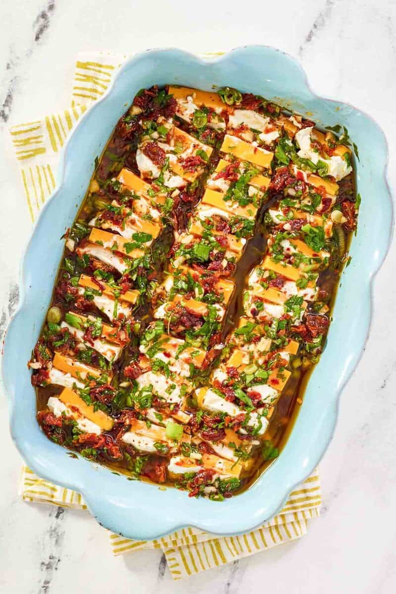 Slices of cream cheese and cheddar cheese with sundried tomato herb marinade in a dish.