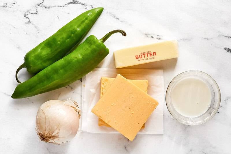 Ingredients for queso including green chile peppers, white onion, butter, orange cheese, and milk.