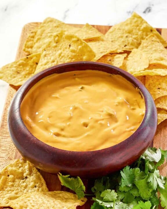 Green chile queso dip, tortilla chips, and fresh cilantro on a platter.