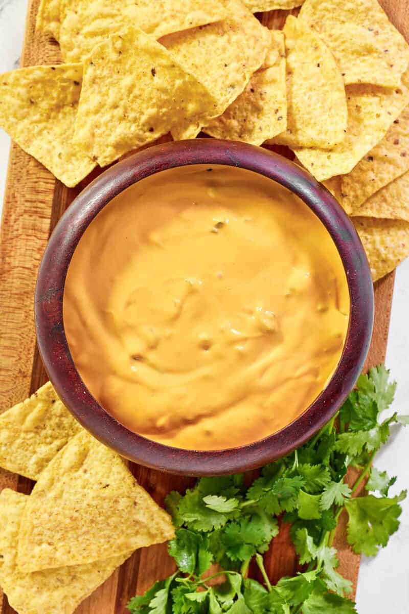 Green chile queso dip and tortilla chips on a wood platter.