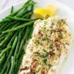 A baked white fish fillet and green beans on a plate.