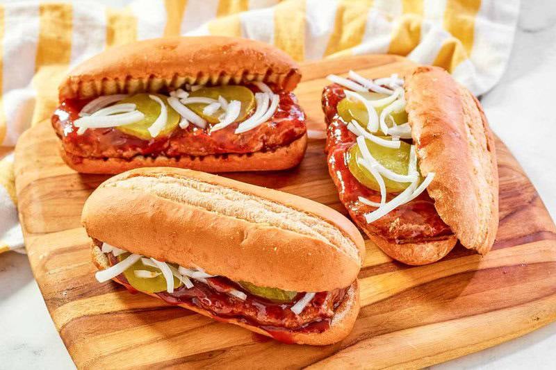 Close-up of three copycat McRib sandwiches showing the pork patty, BBQ sauce, white onions, and pickles.