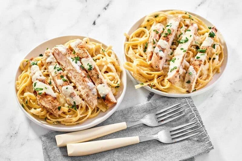 Two servings of creamy chicken fettuccine Alfredo garnished with parsley