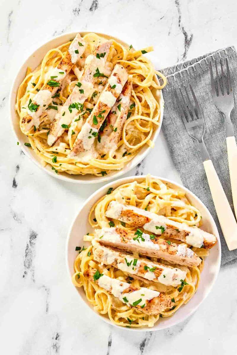 An overhead shot of two bowls of chicken Alfredo pasta with creamy white sauce