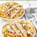 Two plates of homemade Olive Garden chicken alfredo and two forks next to them.