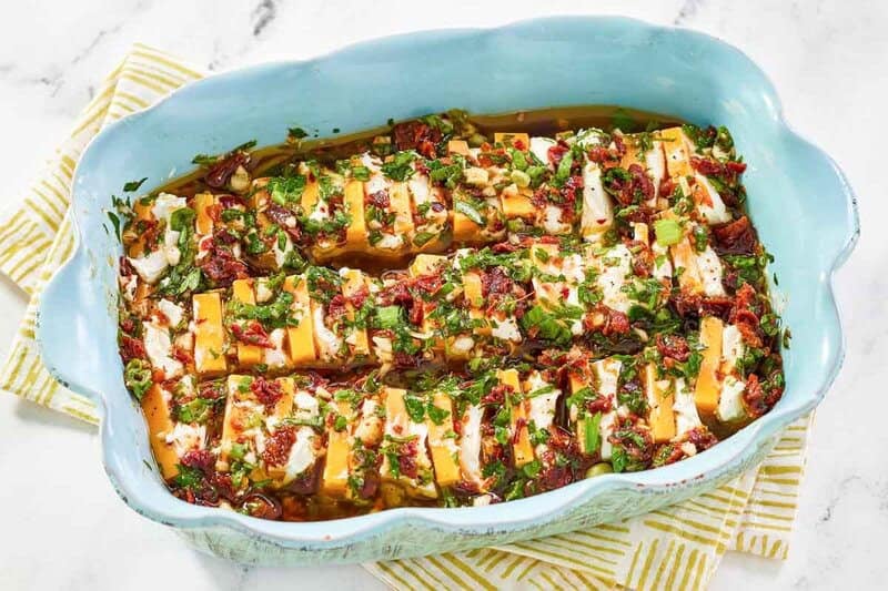 An appetizer of sliced cheeses in tomato garlic herb marinade.