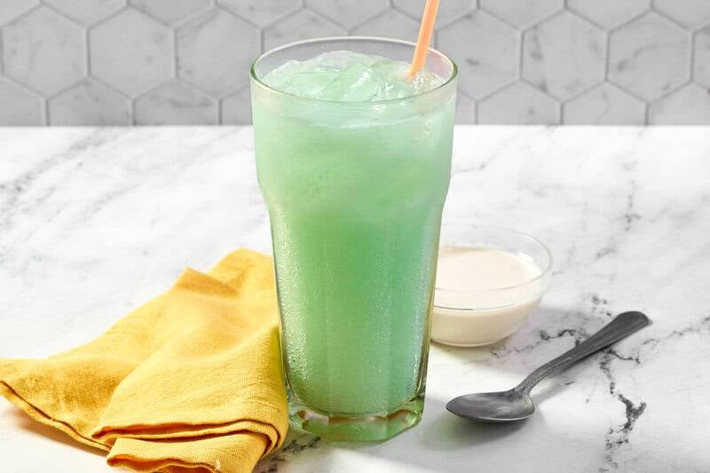 Close up of a frosty Dirty Mountain Dew Baja Blast drink with ice and a peach straw, served with sweet cream.