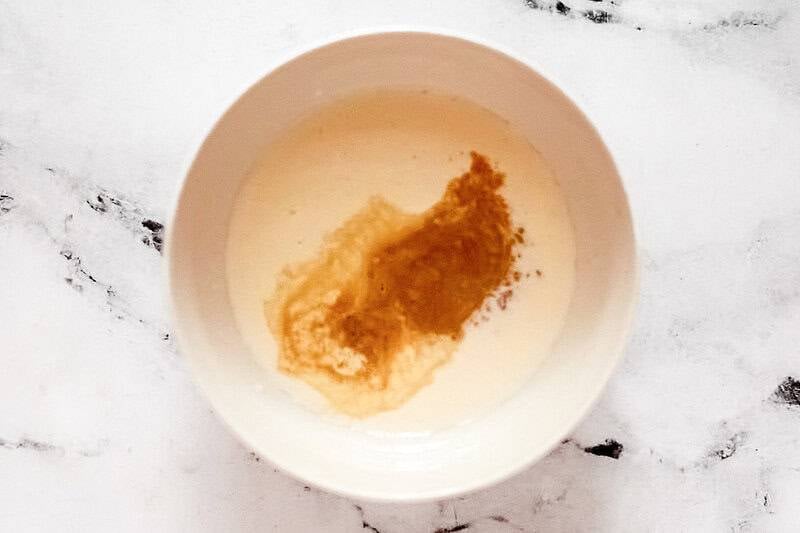 A white bowl containing a cream mixture with dark vanilla extract swirling into it for the soda base.