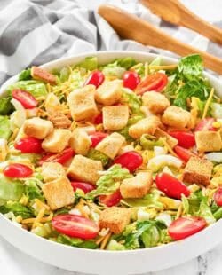 A bowl of copycat Texas Roadhouse house salad and salad tongs on a marble surface.
