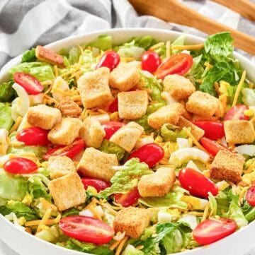 A bowl of copycat Texas Roadhouse house salad and salad tongs on a marble surface.
