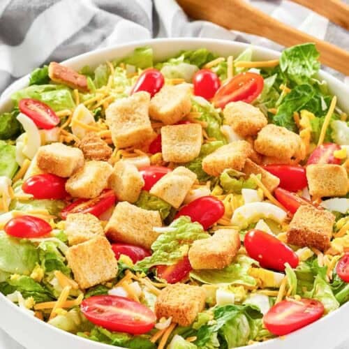 A bowl of copycat Texas Roadhouse house salad and salad tongs on a marble surface.
