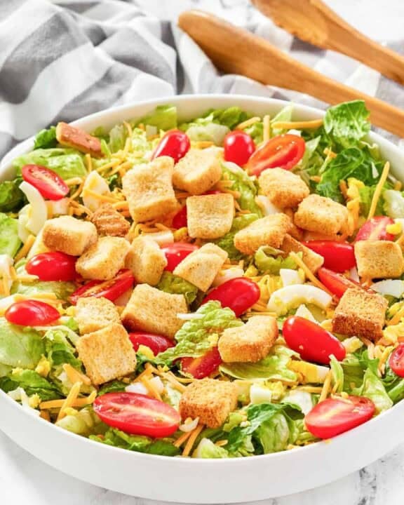 A bowl of copycat Texas Roadhouse house salad and salad tongs on a marble surface.