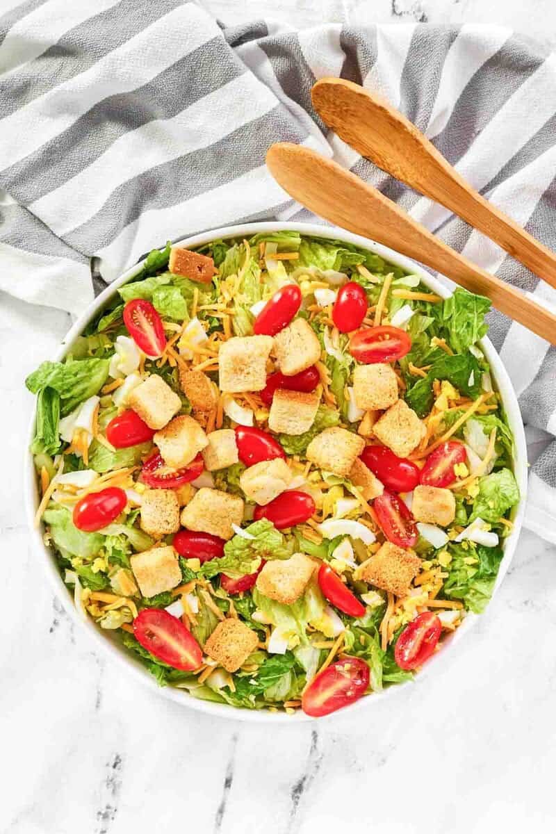 Copycat Texas Roadhouse house salad, salad tongs, and a kitchen towel on a marble surface.