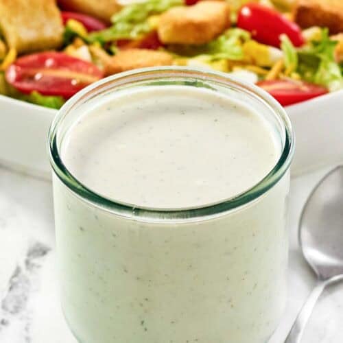 Copycat Texas Roadhouse ranch dressing in a jar and a salad behind it.