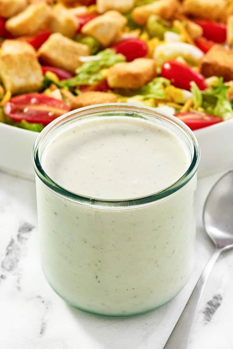 A jar of creamy ranch dressing and a salad behind it.