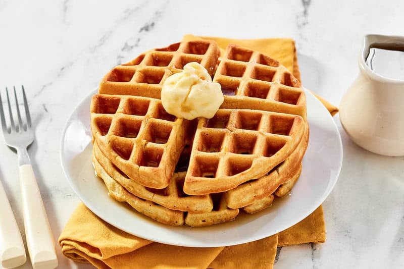 A stack of Waffle House-style buttermilk waffles with butter and syrup on a plate.
