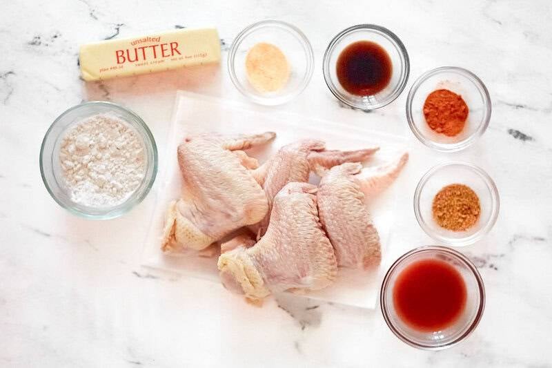 raw chicken wings, butter, flour, hot sauce, garlic powder, spices, and vinegar arranged on a white surface