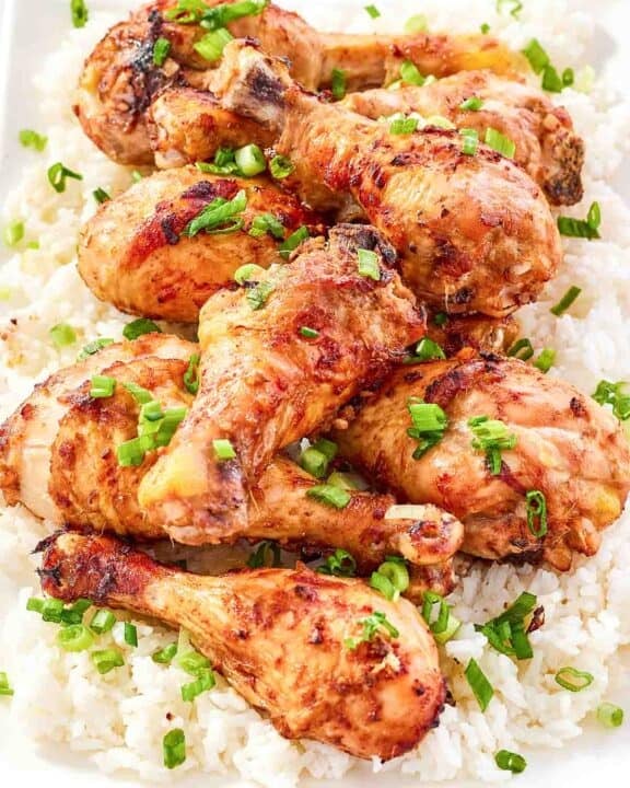 Baked and glazed chicken drumsticks served on top of rice and garnished with green onions.